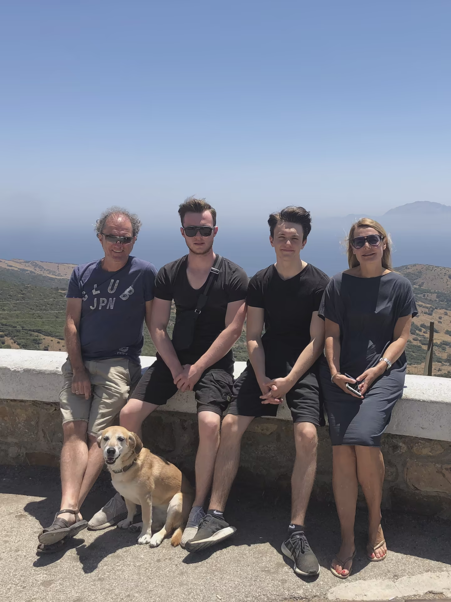 Die Familie mit Hund Madi auf einer Mauer an der K&uuml;ste, dahinter das Meer