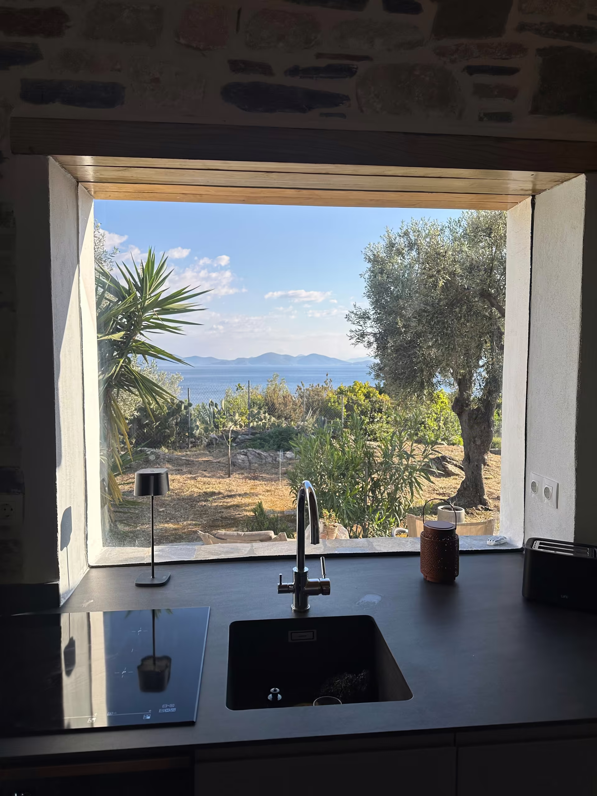 Blick durchs K&uuml;chenfenster auf Olivenbaum und Meer