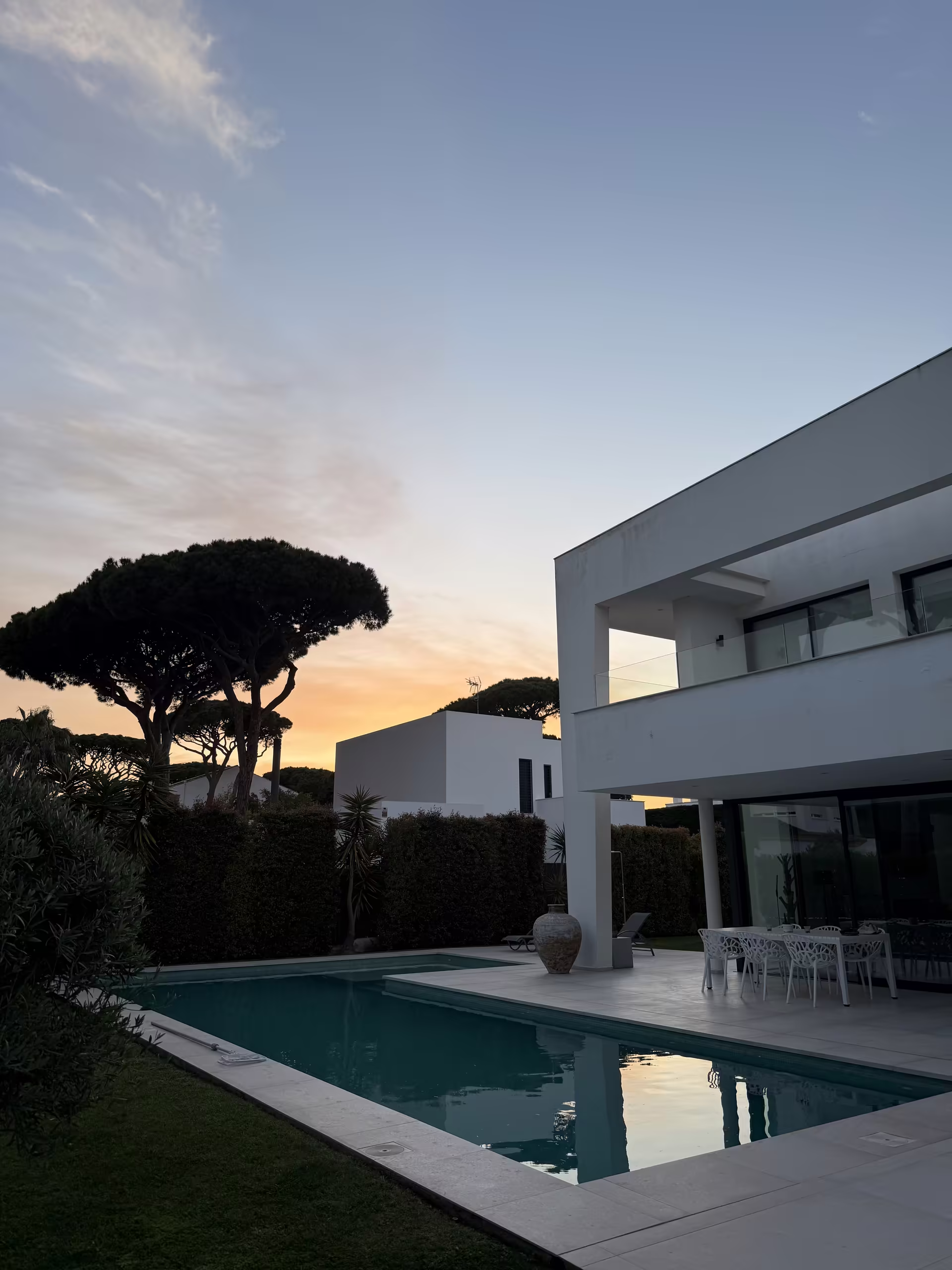 Pool und Villa unter dem Abendhimmel, daneben eine Schirmpinie