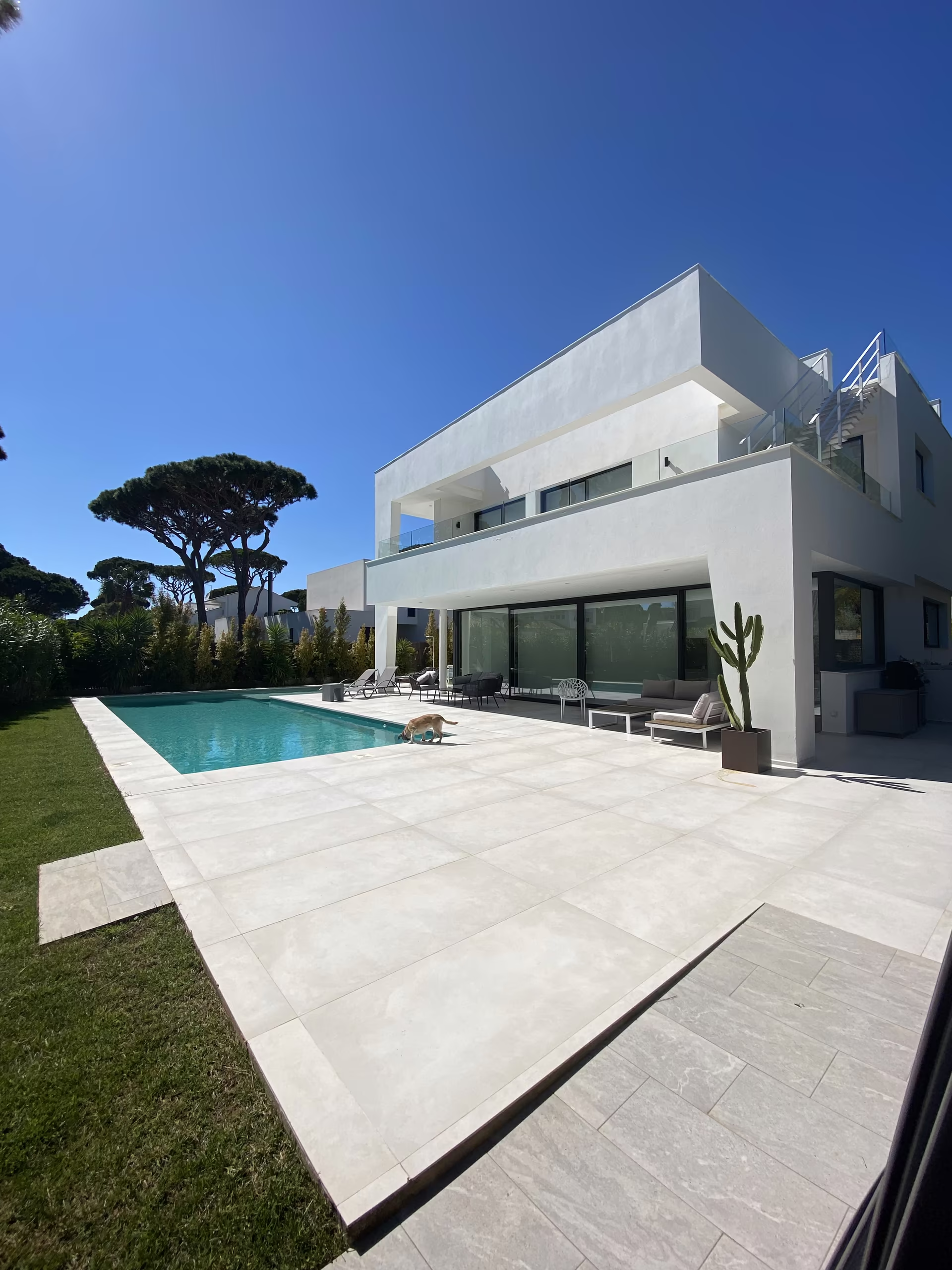 Die Villa von der Gartenseite, davor Rasen, Pool und Schirmpinien