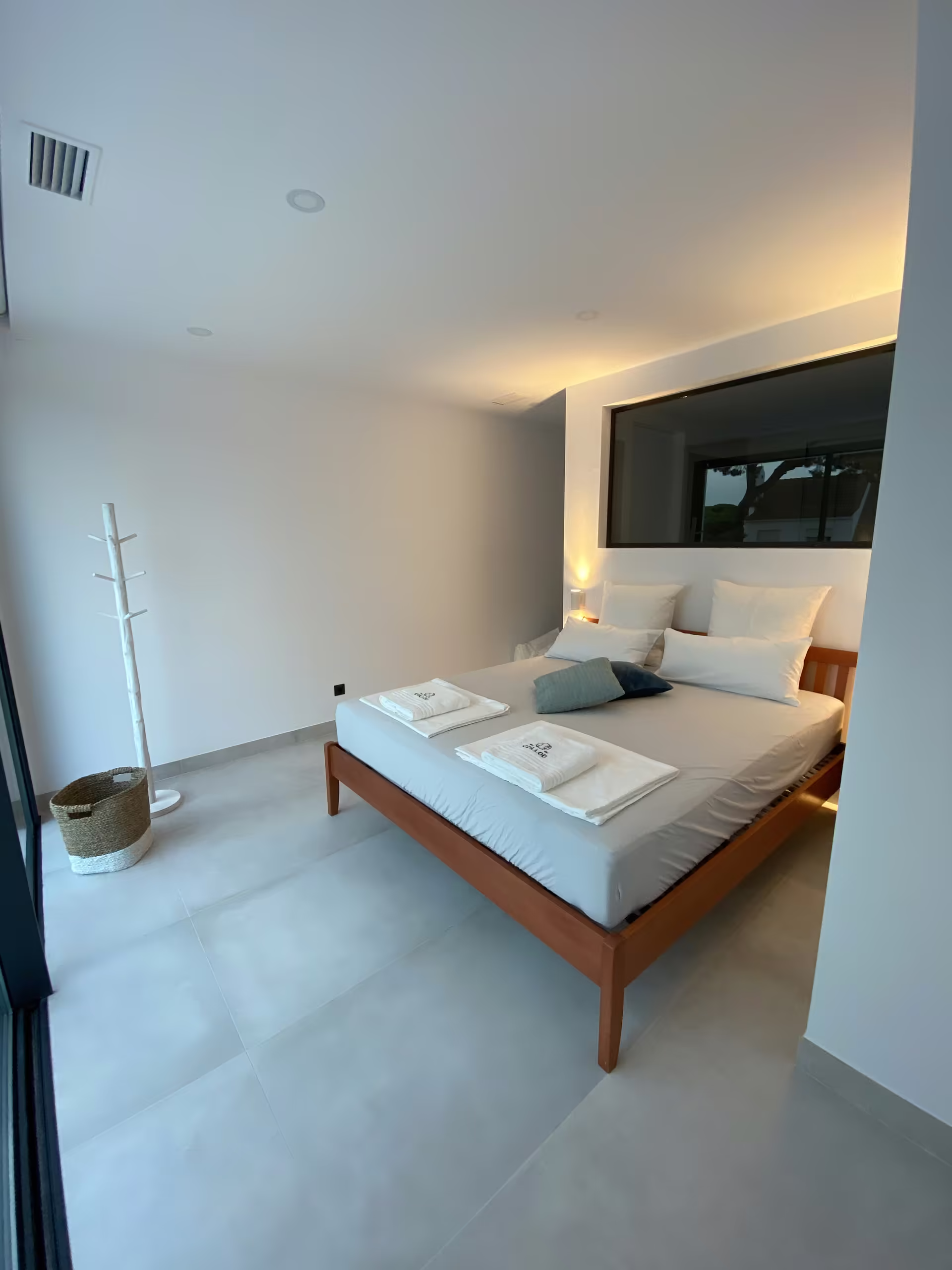 Schlafzimmer mit Holzbett, warmem Licht und Fenster zum Garten