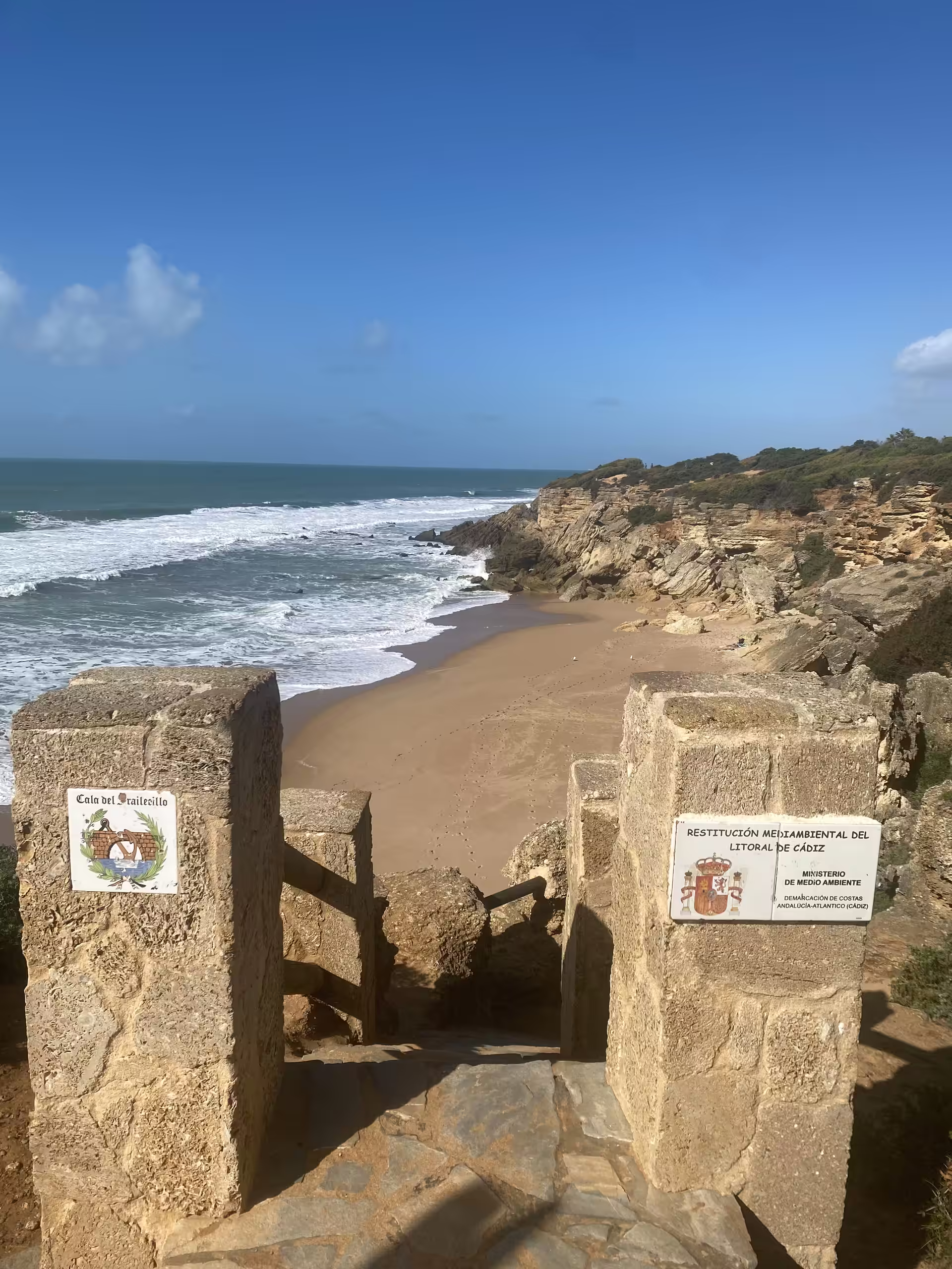 Steinerner Zugang zur Bucht, dahinter Sandstrand und Atlantik