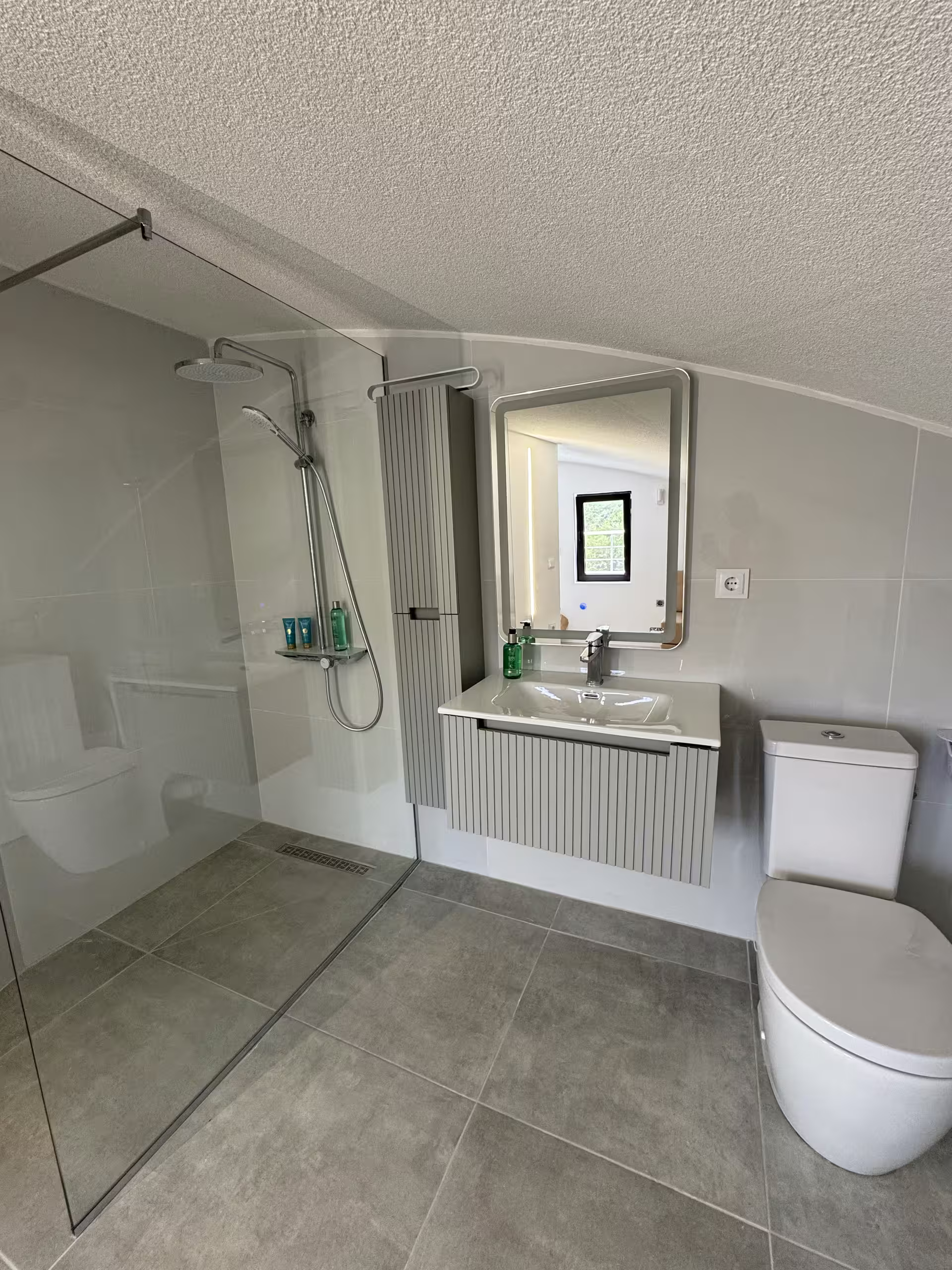 Bad mit bodengleicher Dusche hinter Glas, Waschtisch mit beleuchtetem Spiegel und WC