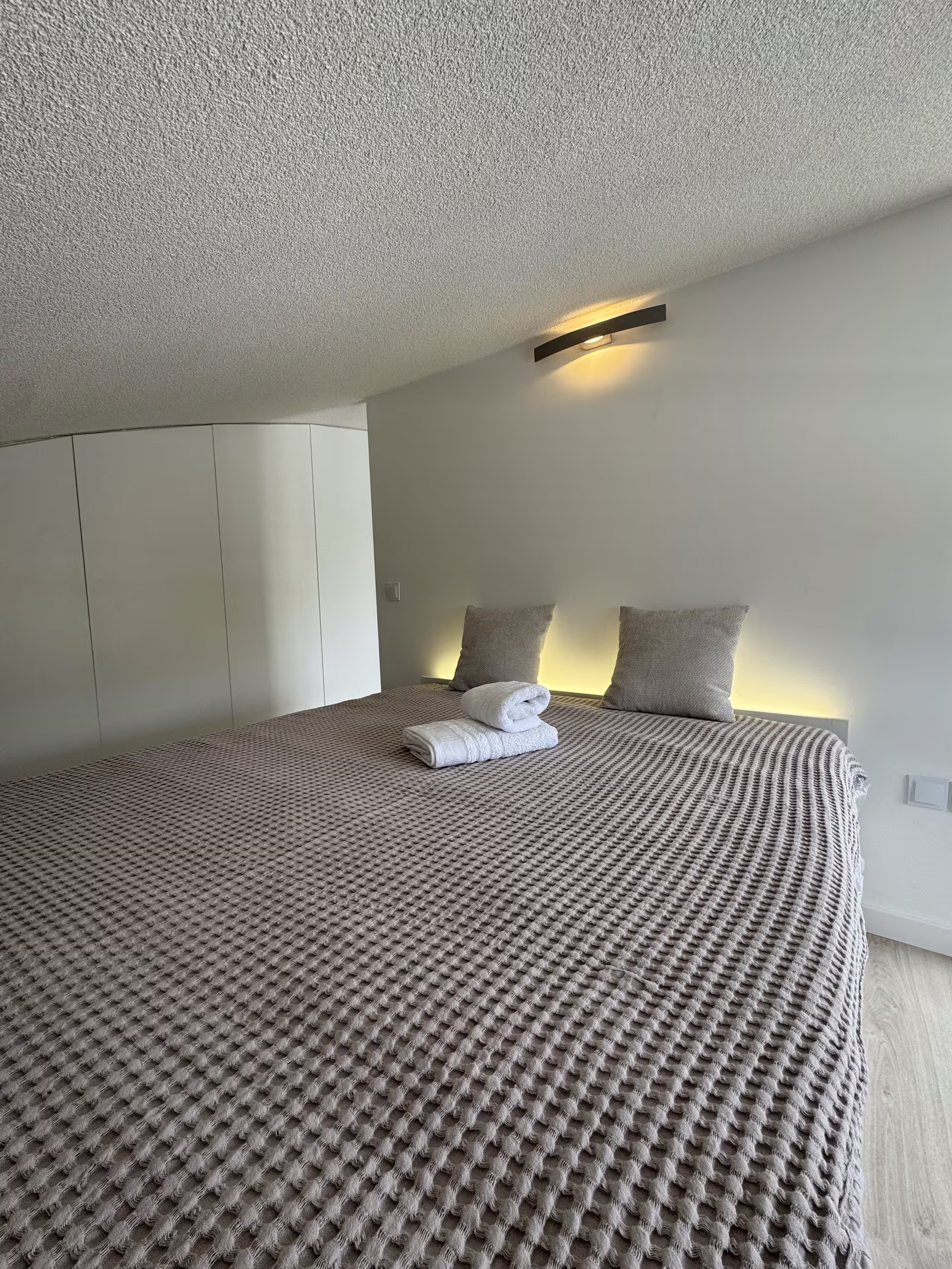 Doppelbett mit gemusterter Tagesdecke, Morgenlicht durch das Fenster