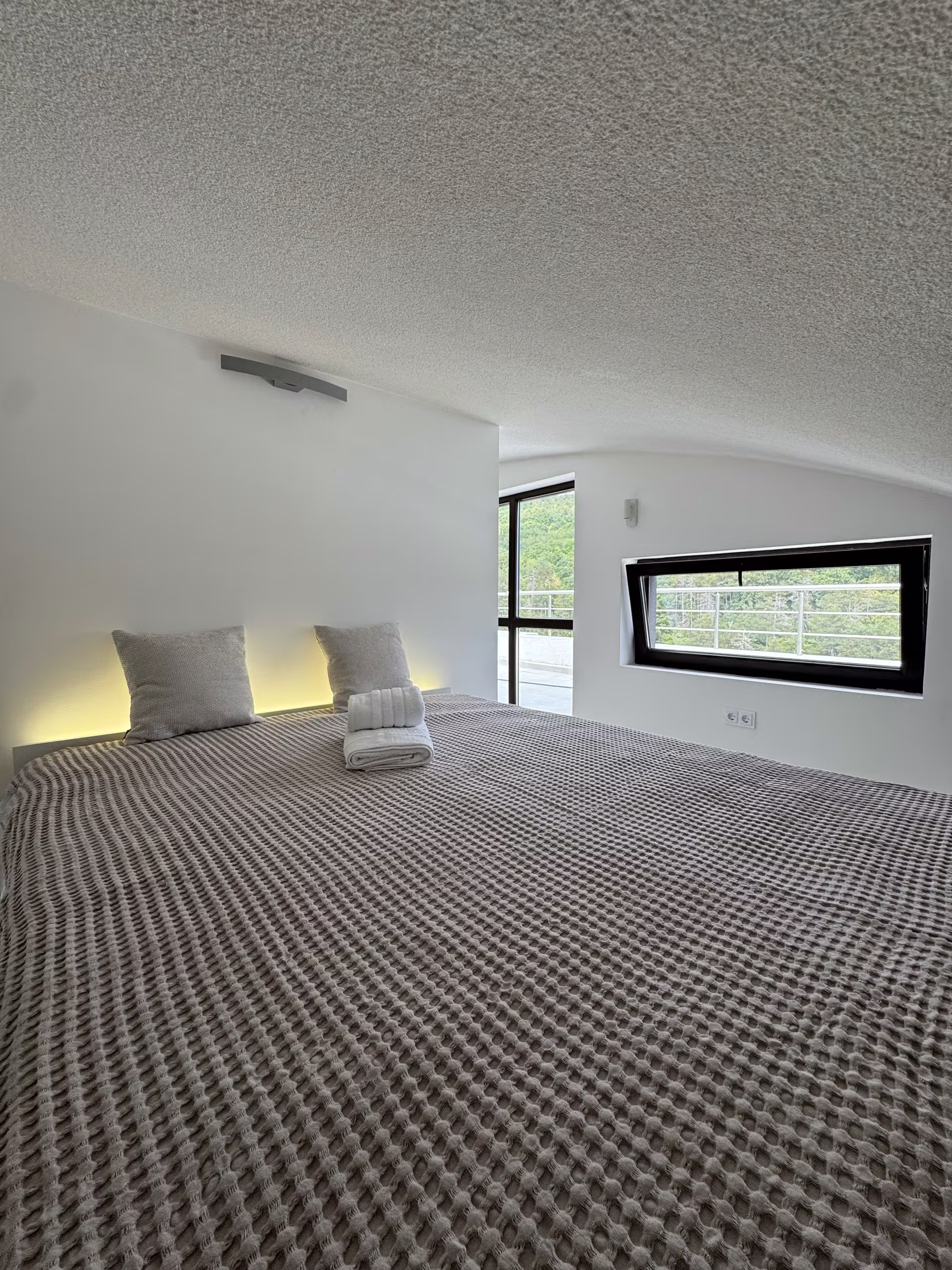 Doppelbett unter der Dachschr&auml;ge, daneben ein liegendes Fensterband