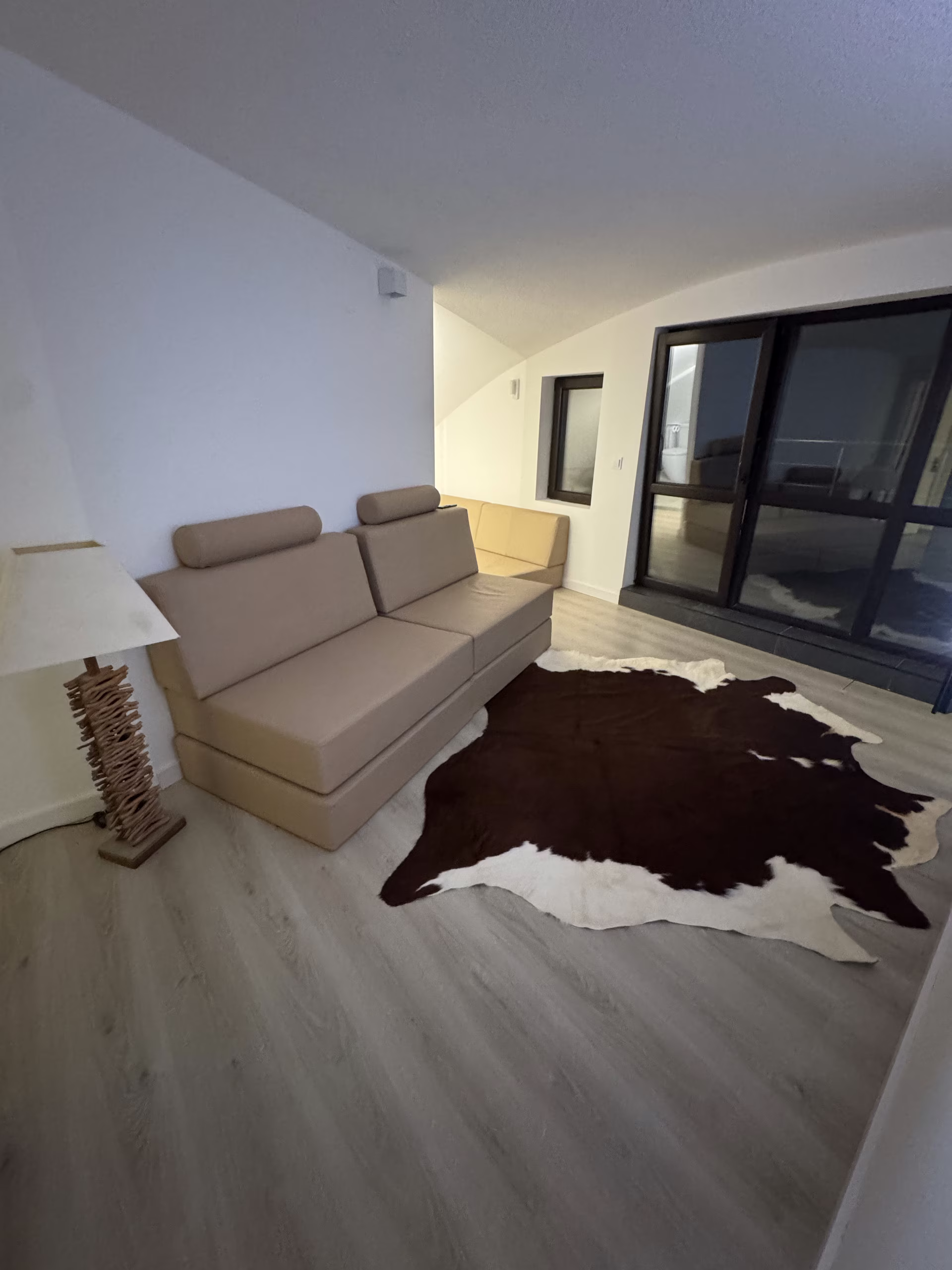 Wohnraum am Abend, Sofa und Kuhfell-Teppich vor der dunklen Fensterfront