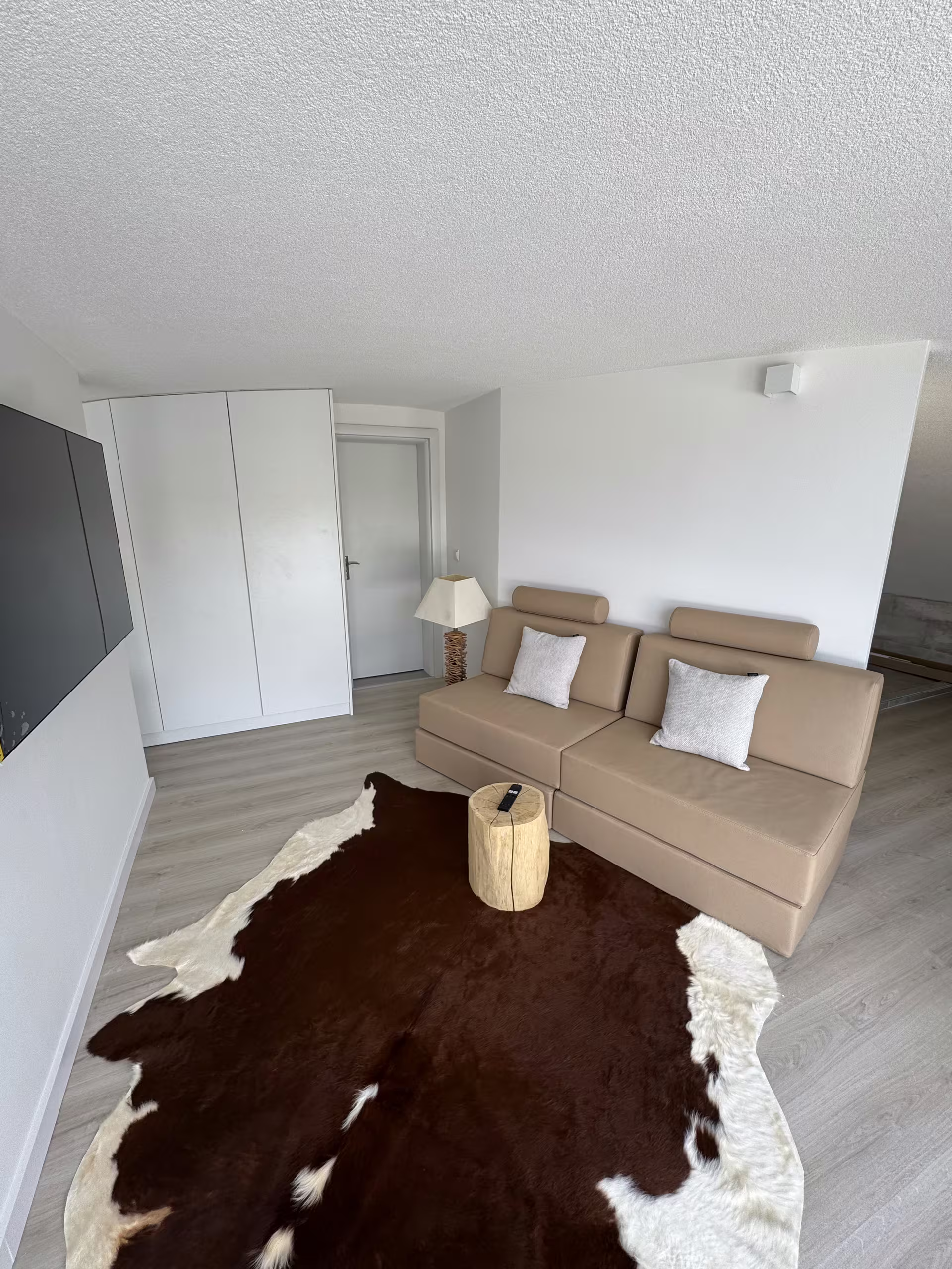 Heller Wohnraum unter der Dachschr&auml;ge mit beigem Sofa, Kuhfell-Teppich und wei&szlig;en Einbauschr&auml;nken