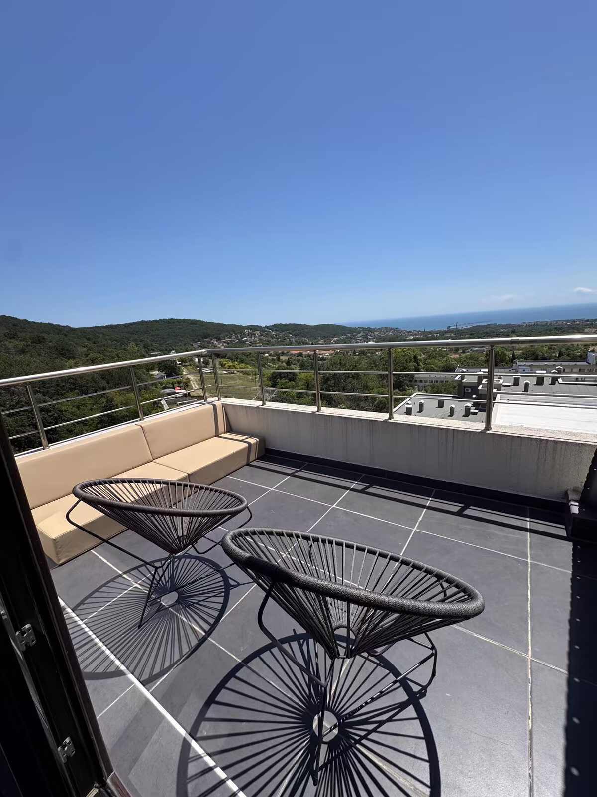 Dachterrasse mit zwei Korbst&uuml;hlen und weitem Blick &uuml;ber das Land bis zum Meer
